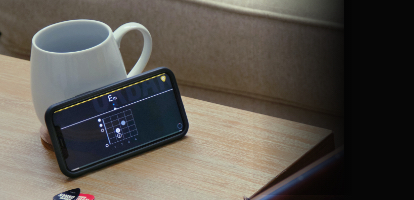 A person practicing guitar using the Urban App on their phone sitting on a coffee table.