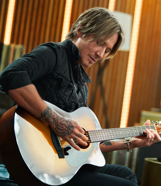 A person practicing guitar using the Urban App on their phone sitting on a coffee table.