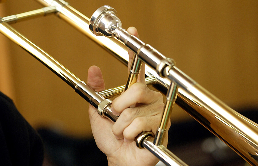 A trombone is held with the left hand and played with the right hand