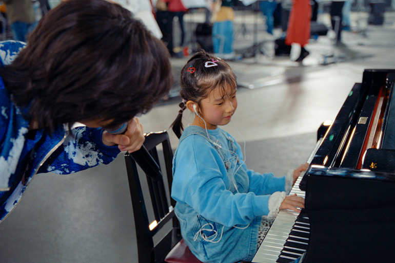 [Photo] imase singing while approaching a young girl playing the piano.
