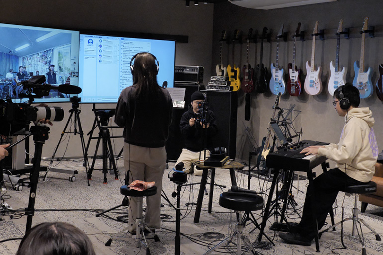 [Photo] Participants in a studio and online musicians rehearsing together using SYNCROOM.