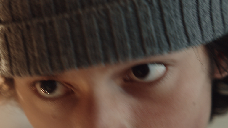 [Photo] Close-up of a person’s eyes beneath a knit cap, with the face tightly framed and background softly blurred.