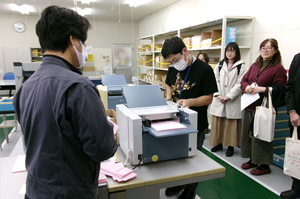 [Photo] Employees observing envelope filling and sealing process