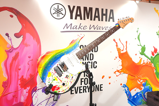 [ 画像 ] ヤマハのブースに立つ従業員ボランティア、展示楽器、取り組み紹介パネル