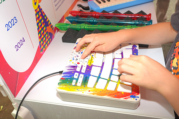 [ 画像 ] ヤマハのブースに立つ従業員ボランティア、展示楽器、取り組み紹介パネル