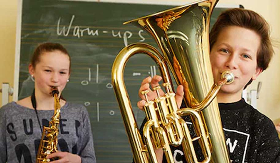 [写真] 音楽室でサックスとユーフォニアムを持ち、笑顔でポーズをとる2人の生徒。