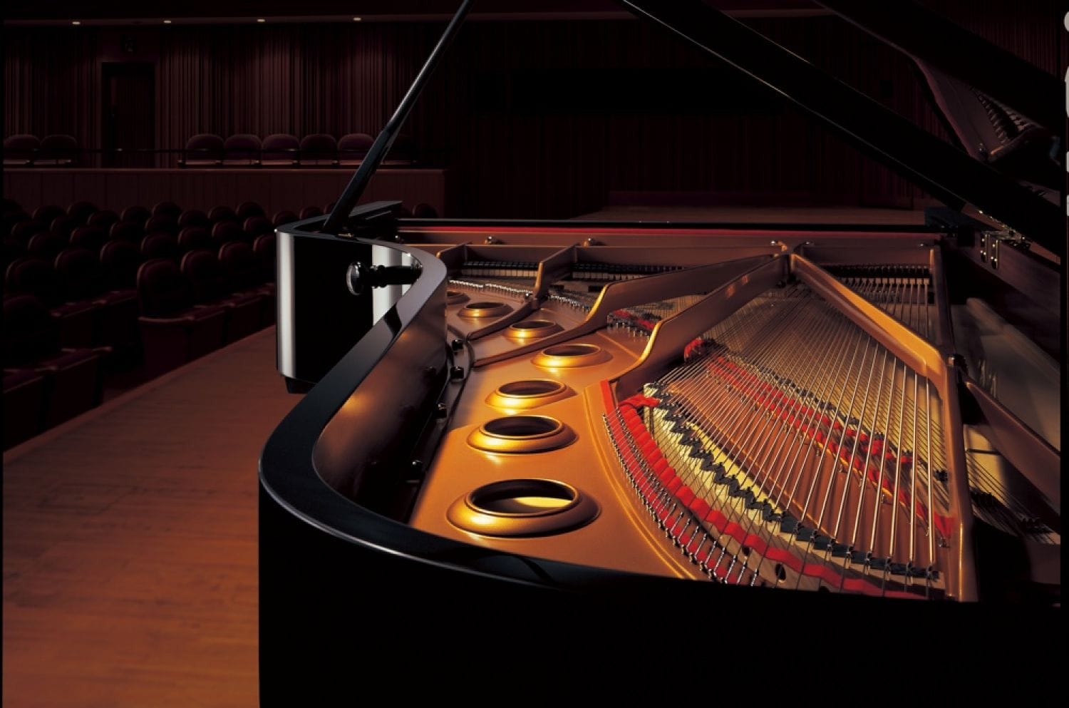 View of interior of a Yamaha concert grand on stage in an empty concert hall.