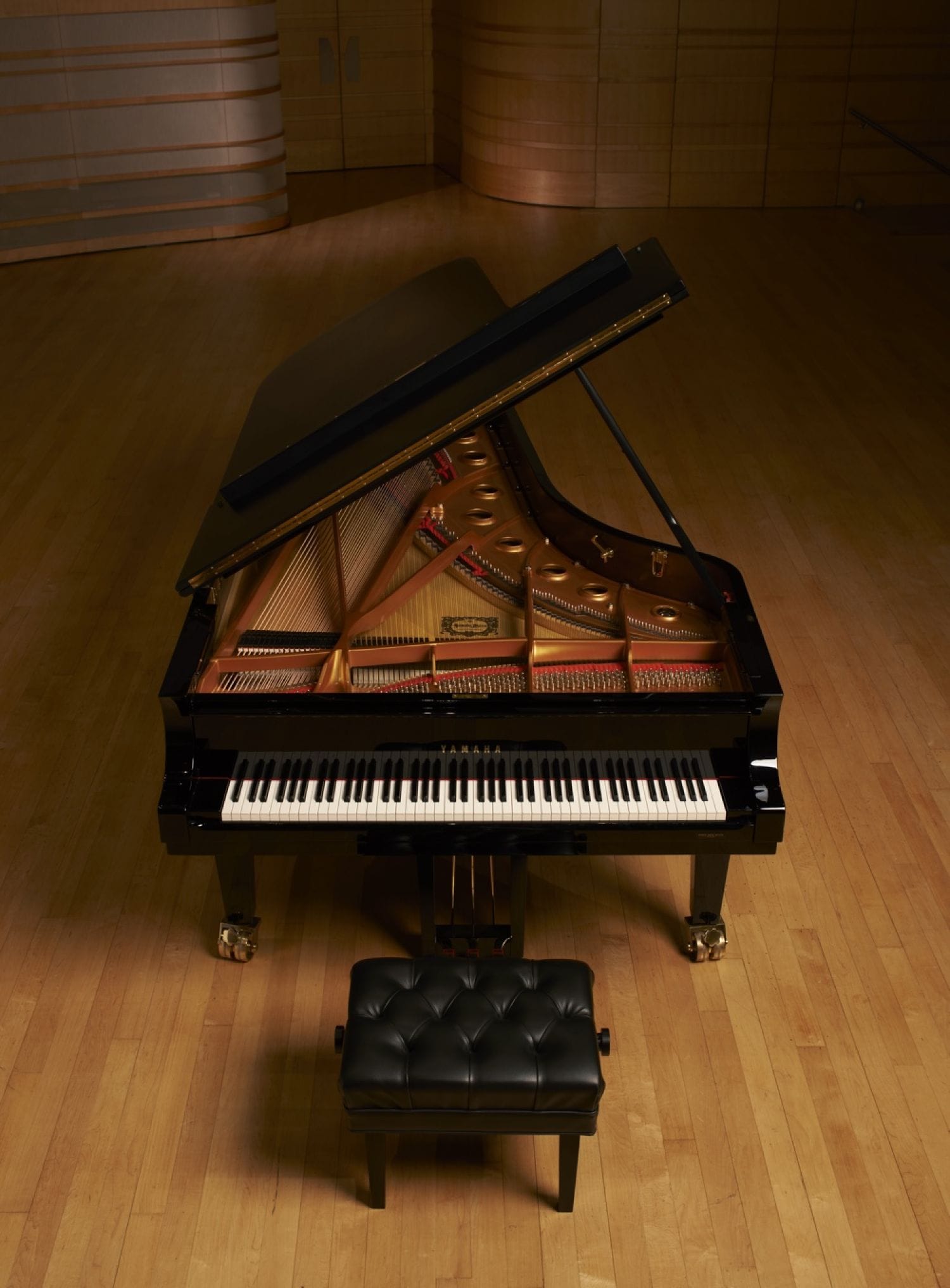 A view of a Yamaha concert grand with the lid open and view of keys and inner workings on an otherwise empty stage.