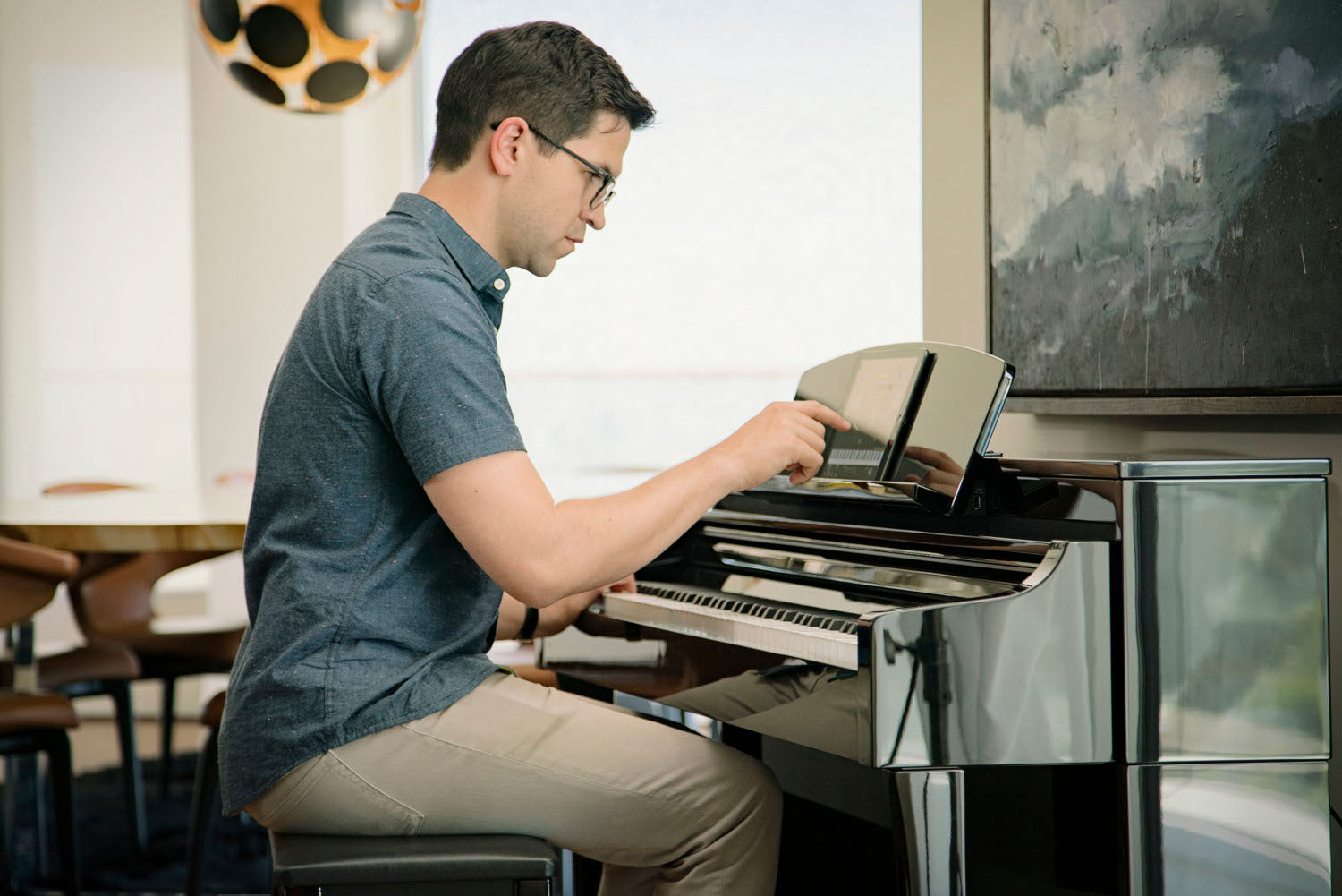A man approximately 40 years old is smiling broadly while playing from sheet music on a Yamaha upright piano in a living room setting.