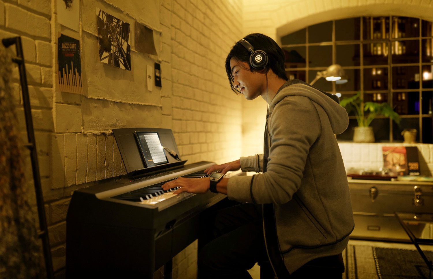 A man approximately 40 years old is smiling broadly while playing from sheet music on a Yamaha upright piano in a living room setting.