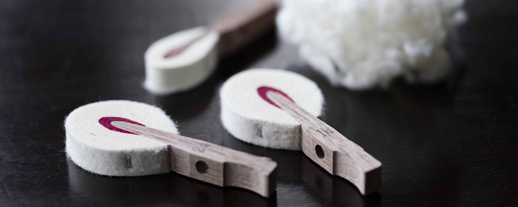 Individual piano hammers which are small pieces of wood with one end wrapped in felt with a handful of felt in the background.