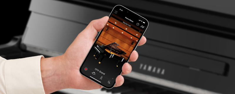 hand holding a mobile phone with a piano on a background