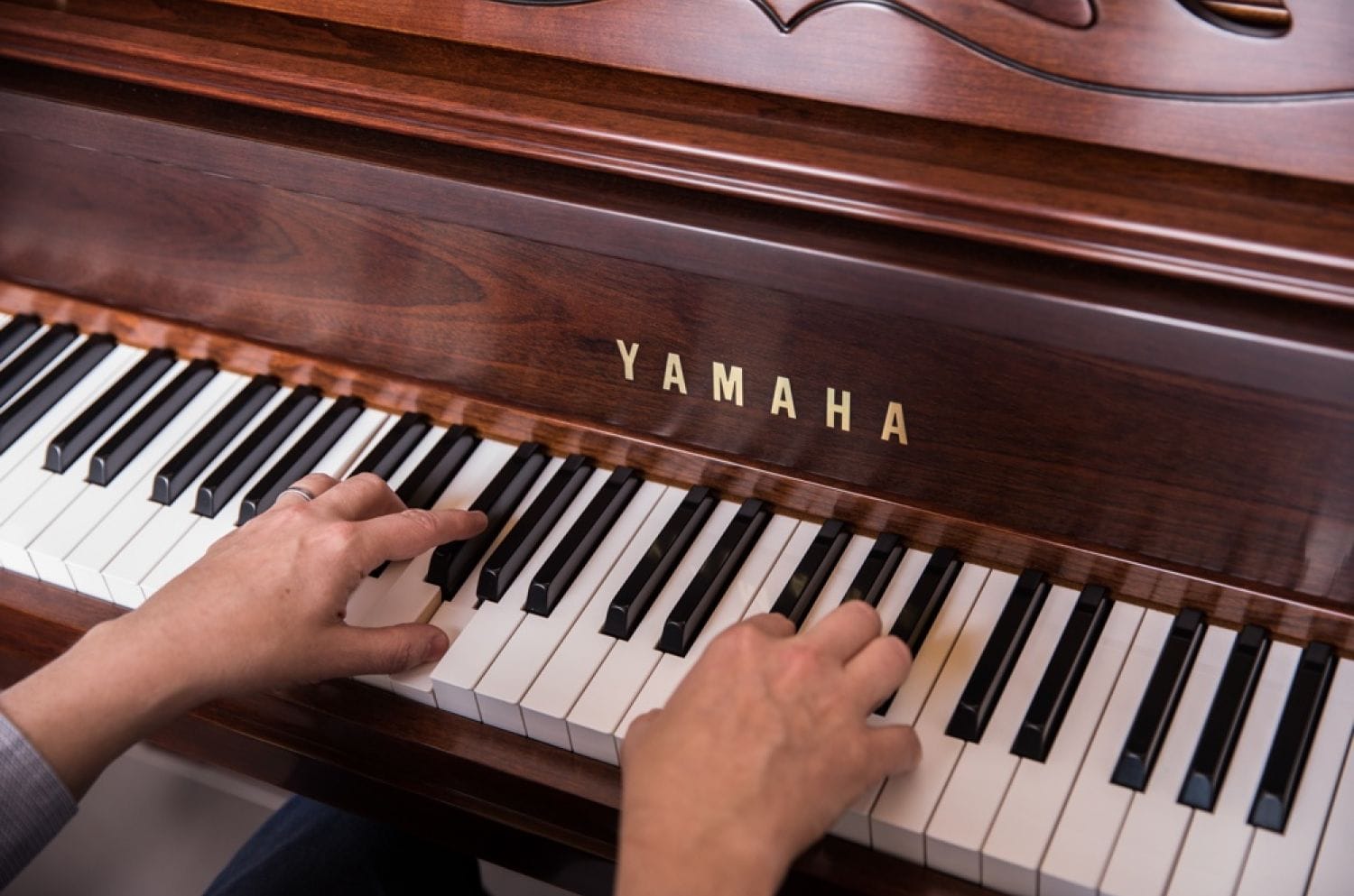 Young adult's hands playing a Yamaha upright Gallery piano.