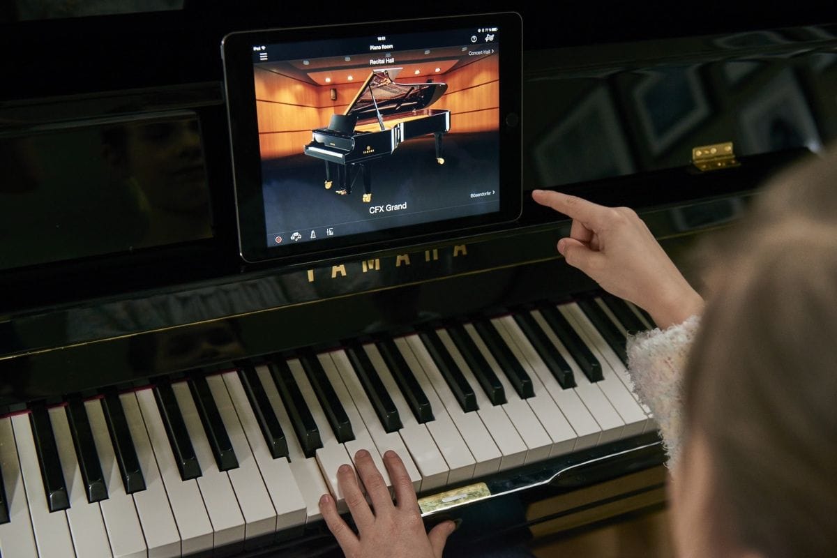 Young woman playing a Yamaha piano with a tablet-style screen above the keyboard which is providing information on the CFX Grand piano.