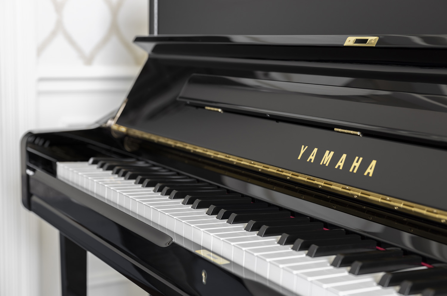 Side view from above of a young girl playing an upright piano that has framed family photos on back in a corner full of windows covered with lightweight sheer drapes.