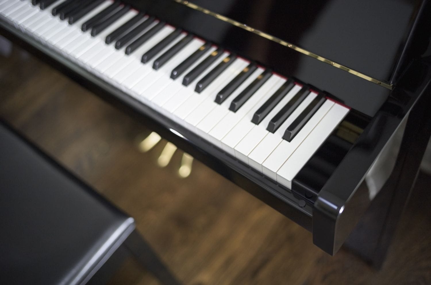 Closeup of right hand side of piano keys and bench.