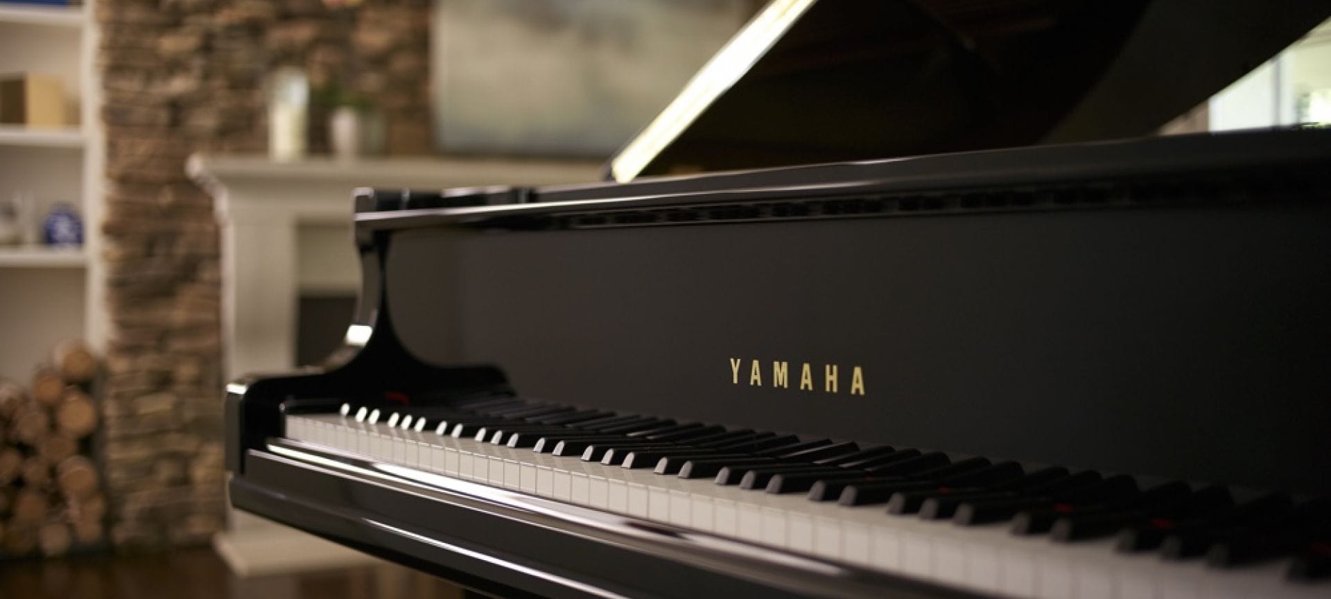 Close-up of Yamaha baby grand piano keys with lid open and fireplace in background.