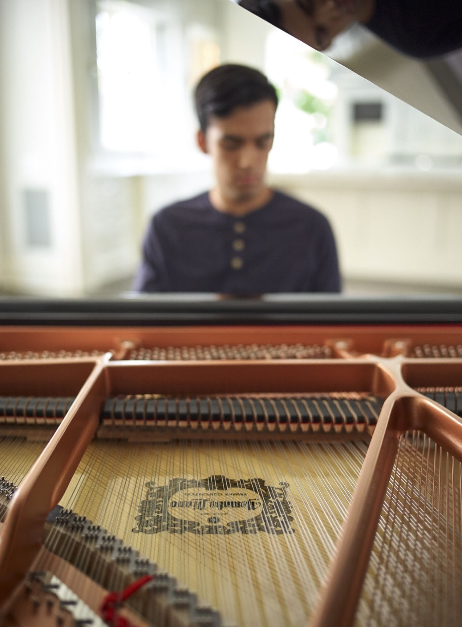 Closeup of the inner workings of the piano with a young man seated at the far end focused on playing.