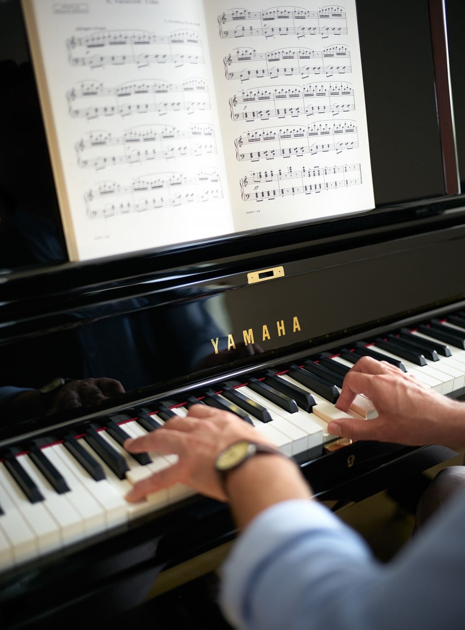 Closeup of man's hands as he plays a Yamaha piano from sheet music.