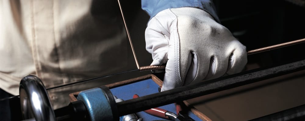 Closeup of gloved hands wrapping a piano wire that is taut.