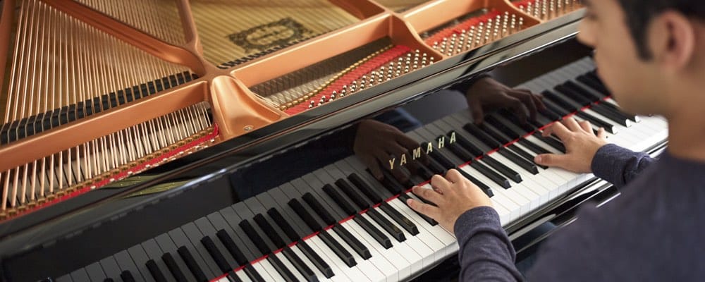 Young man playing a Yamaha baby grand with the lid open to see inside piano.