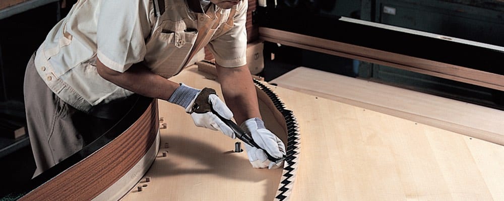 A man in work gloves using a special tool to assemble interior of a piano.