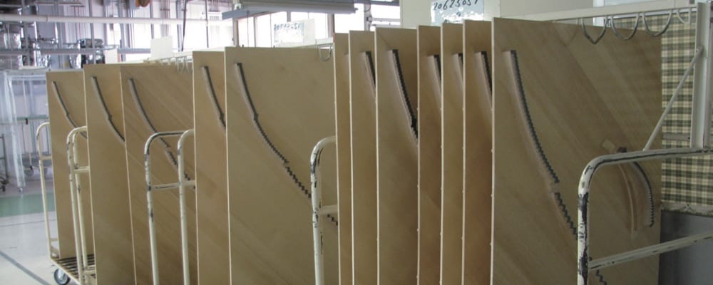 A set of rolling racks in the piano factory with a set of wood soundboards standing vertically with ribs in place.