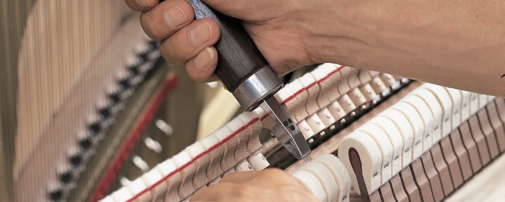 A closeup of a man's hands as he uses a pair of pliers to adjust hammers.