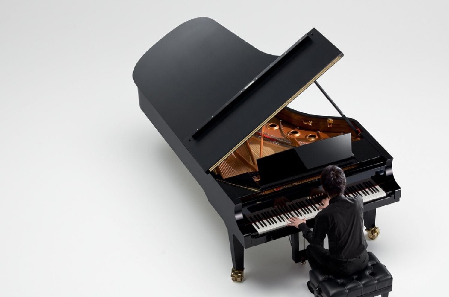 A woman playing a Yamaha concert grand piano with the lid open in a large empty space.