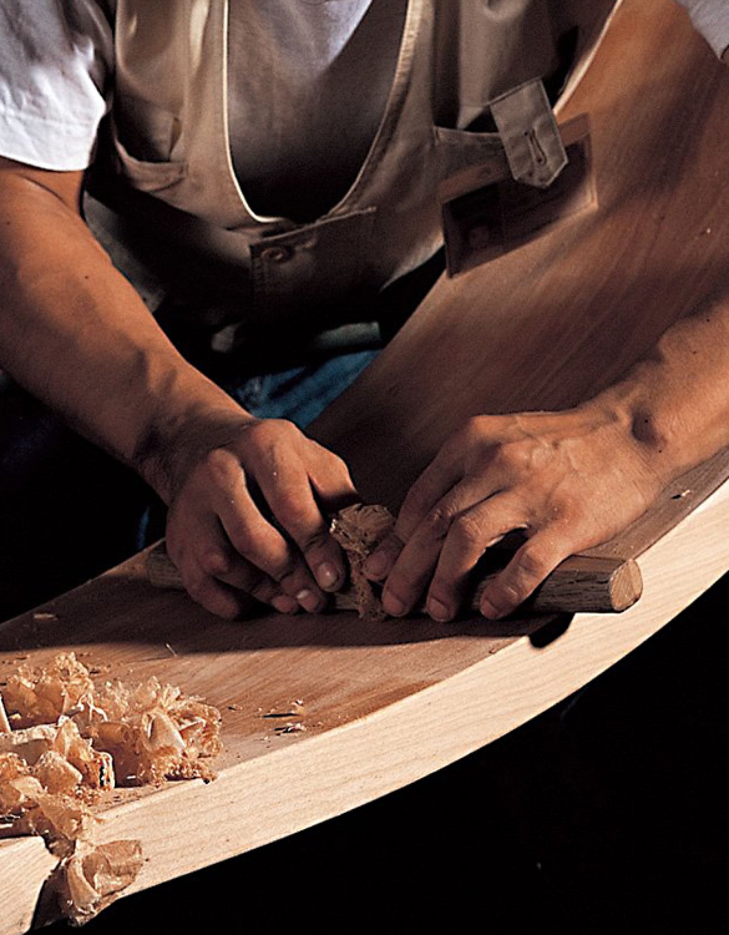 A craftsman's hands as he hand planes the wood for the edge.