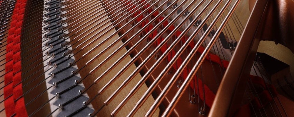 Closeup of bass strings in a finished piano showing that each of the strings are wrapped in …