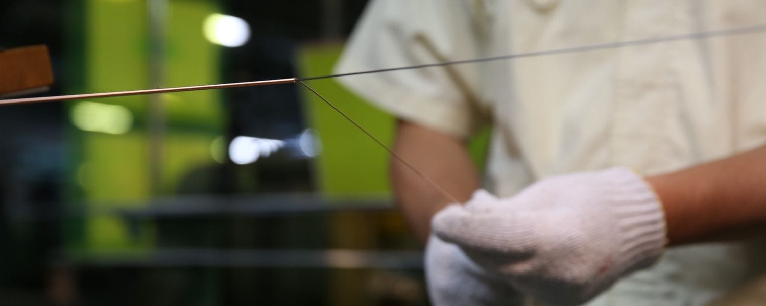 Man wearing short sleeve shirt and knit work gloves handwrapping a piano string that is stretched across foreground.