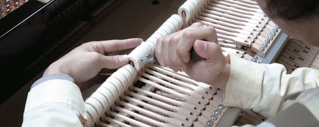 Someone's hands assembling the piano hammers with a small pair of pliers.