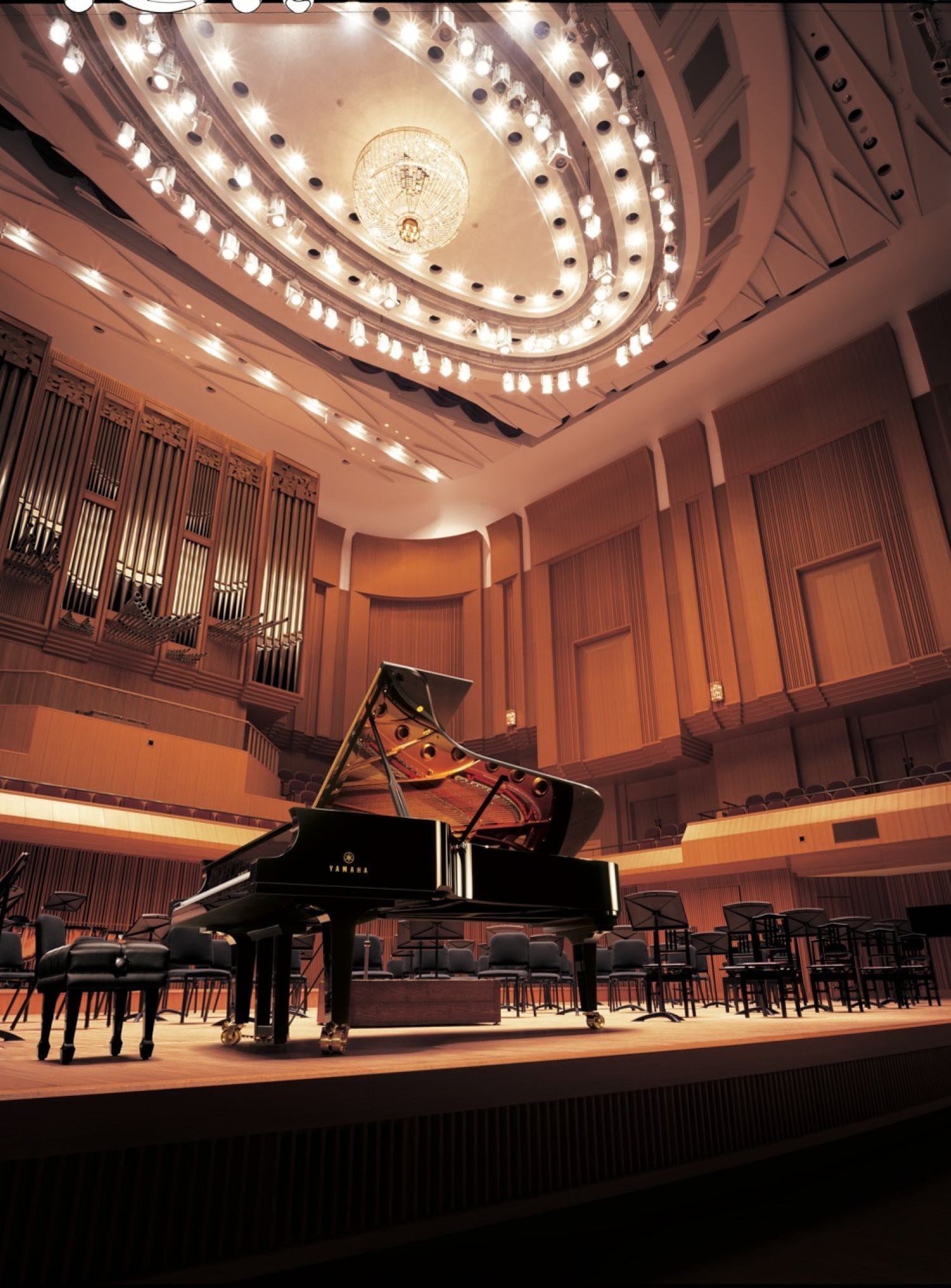 A Yamaha concert grand piano front and center on a fancy performance hall set for an orchestral performance.