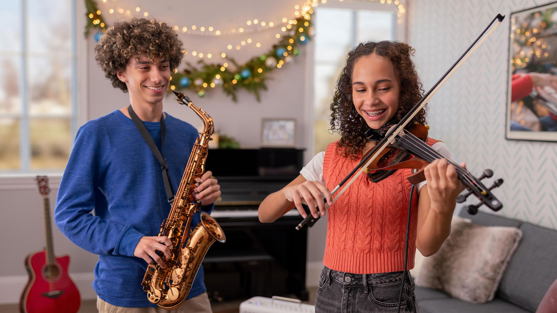 Teenager boy smiling holding the saxophone and girl smiling playing the violin